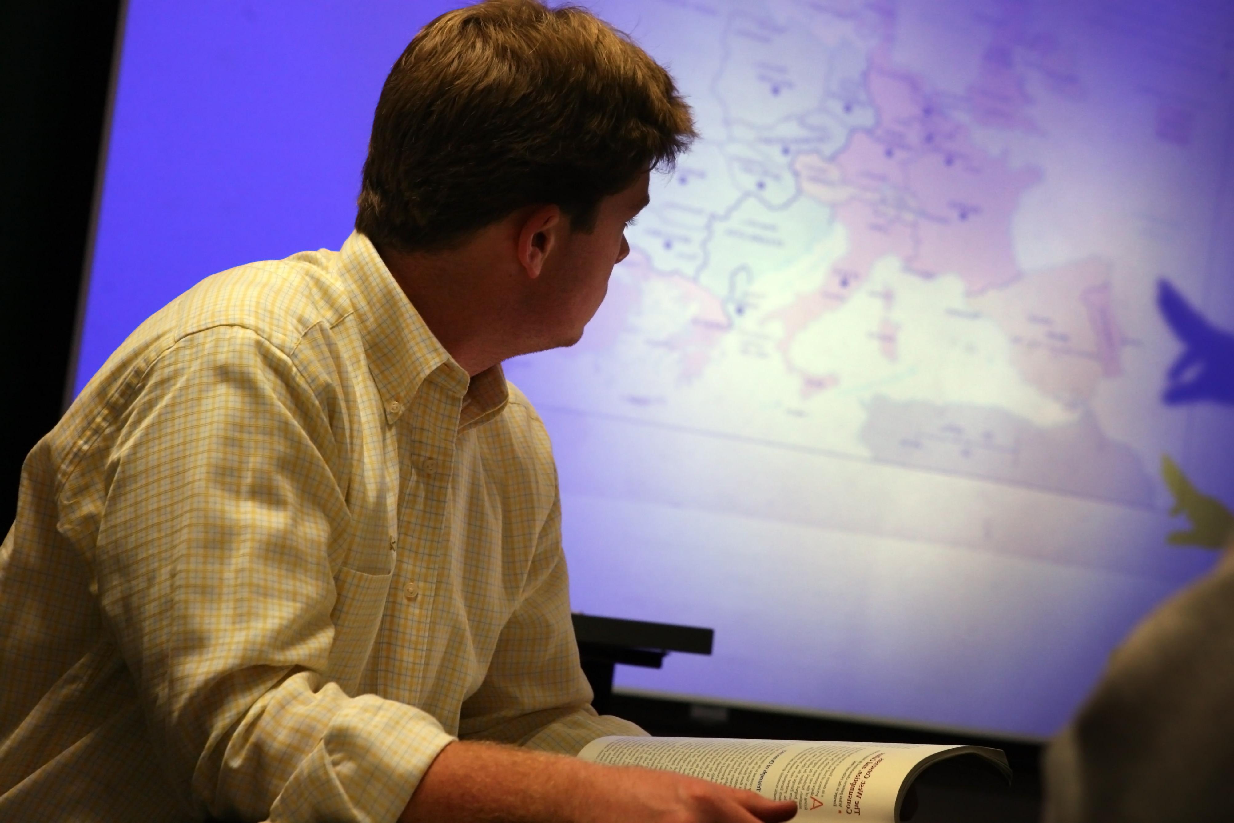 在教室里，一名学生正在研究投影在大屏幕上的地图.